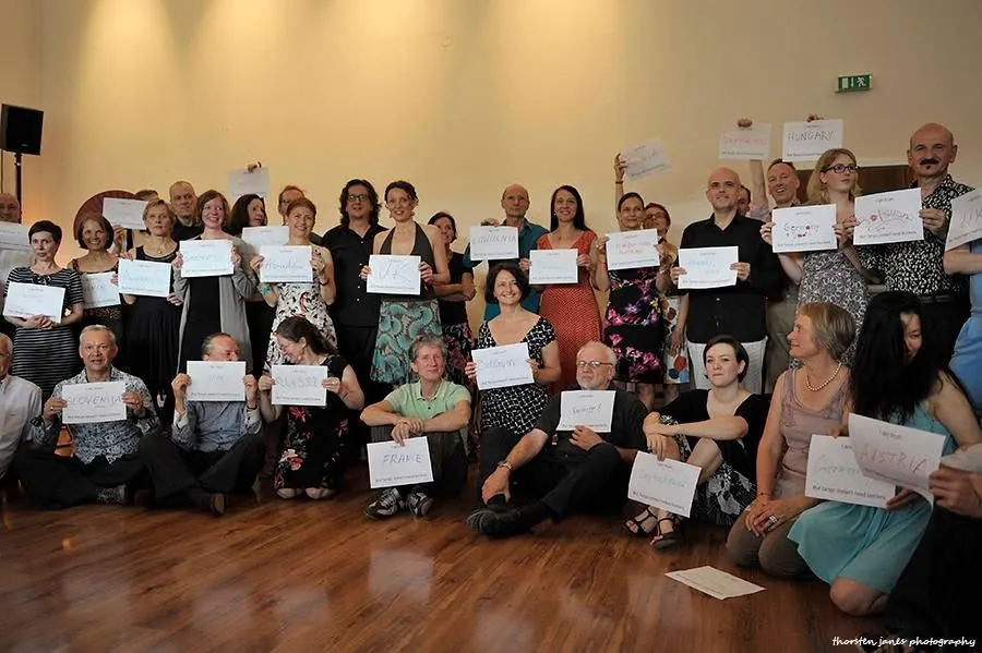 A large group posing for a photo, seated and standing, many holding up handwritten country name signs.