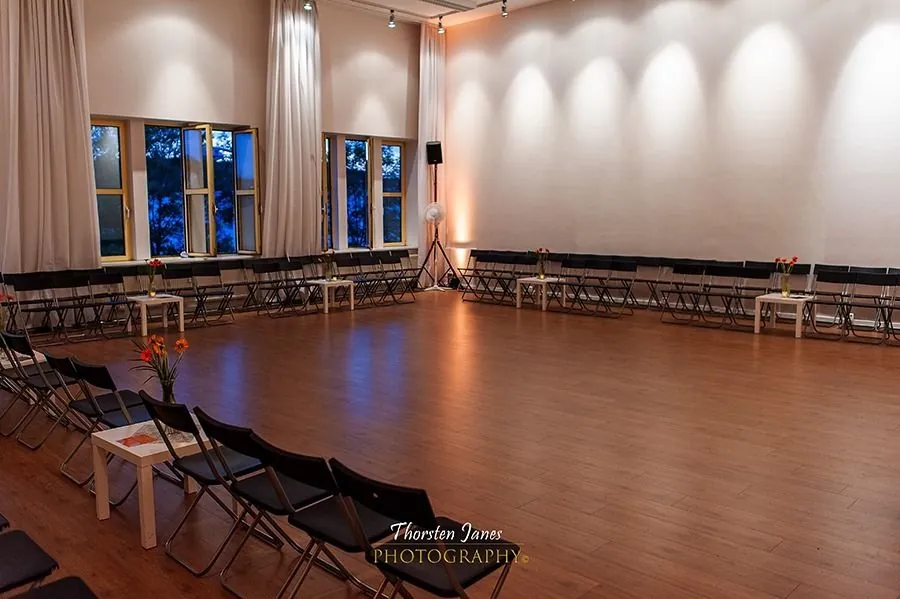 The hall set for an evening event, chairs arranged in a wide ring around an open dance floor with flowers on side tables.