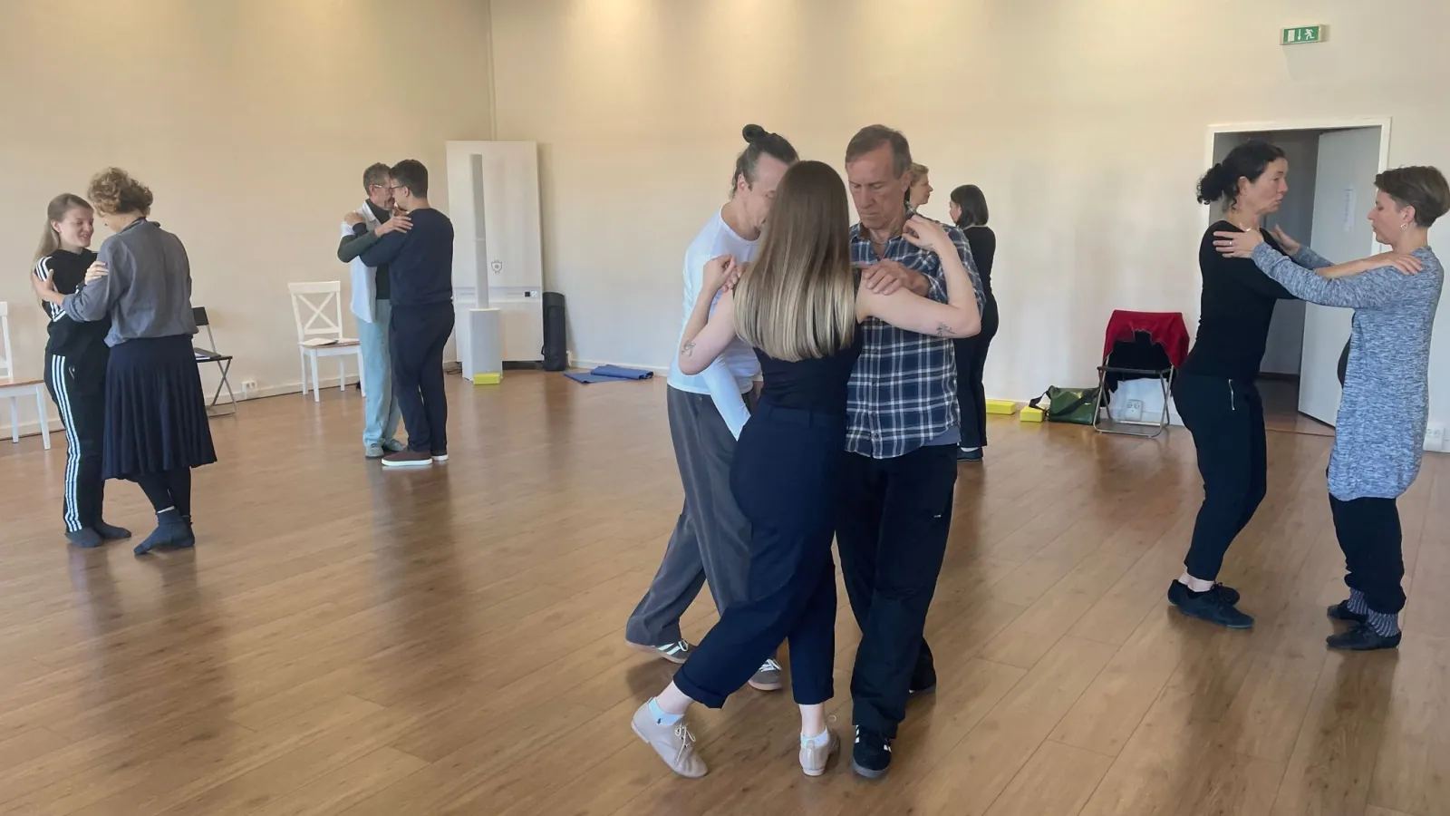Several couples practising tango in a close embrace in the daylit studio, dressed in casual clothes.
