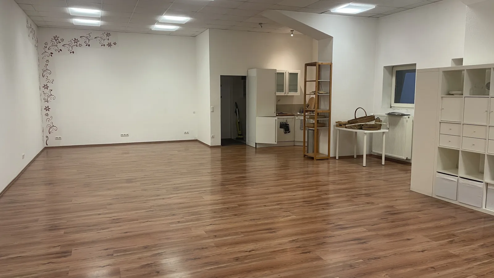 The empty studio from another angle, showing a small kitchenette, open shelving and a decorated wall.