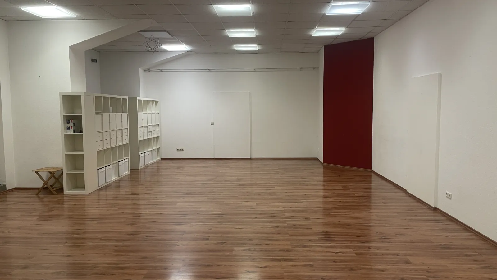 The empty studio with a polished wood floor, white shelving units and a deep red accent wall.